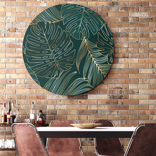 Rundes Akustikbild hängt an einer Backsteinwand im Esszimmer oder Cafe. Motiv ist dunkelgrün mit goldenen Blättern.